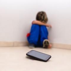 Child sitting against wall upset with a mobile phone on the floor