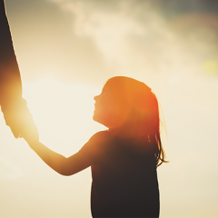 Young child holding adult hand backlit by sun